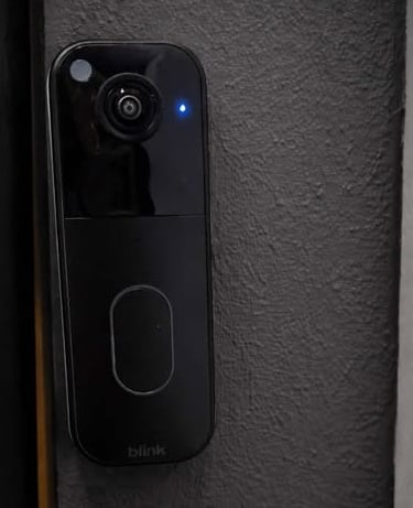 Slim black video doorbell camera mounted beside a door frame with blue status light on