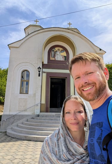 Moose and Bugs taking a selfie in front of a traditional white Orthodox church with golden crosses.