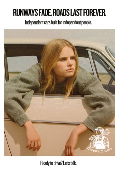 A young blonde woman rests her arms out of the passenger window of a cream-colored vintage car. She wears oversized knitwear 
