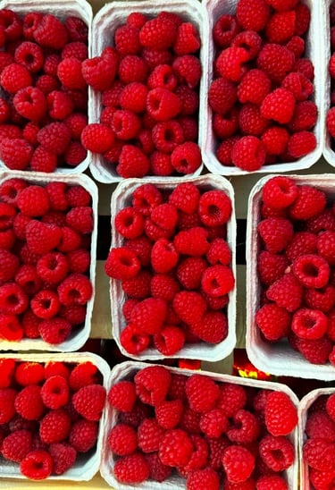 Świeże maliny w plastikowych pojemnikach, gotowe do sprzedaży na targu.