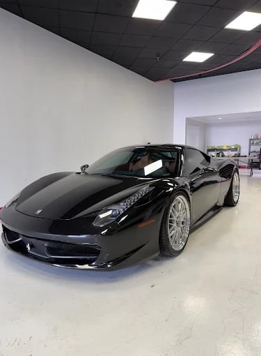 A sleek black Ferrari 458 Italia supercar with silver multi-spoke wheels parked in a luxury automotive showroom.