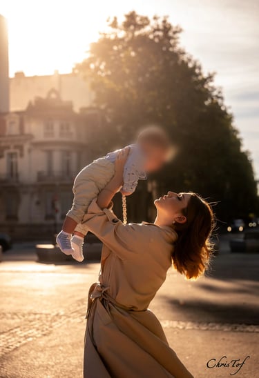 Photographie d'une mère soulevant son bébé dans les airs, au soleil couchant à Perpignan.