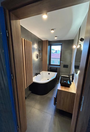 Nowoczesna łazienka z wolnostojącą wanną, drewnianymi panelami na ścianie, czarną umywalką i dużym lustrem.