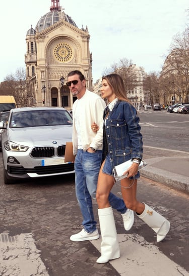 Couple walking in Paris near a cathedral; woman in denim outfit and white boots.