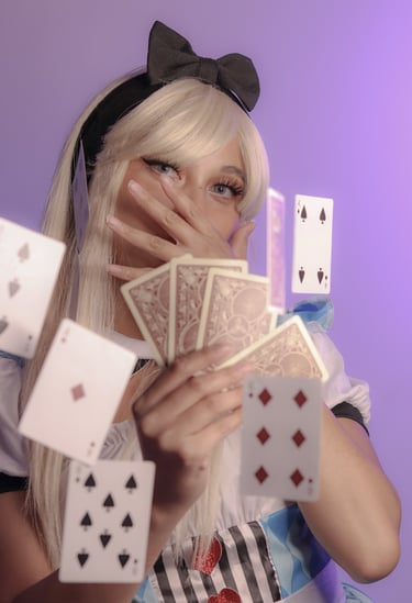 Playful costume of Alice in Wonderland holding playing cards, more cards floating in the air. 