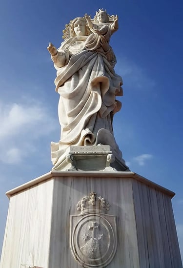 White marble statue of the Virgin Mary holding baby Jesus against a clear blue sky background.
