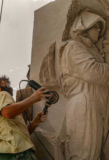 Professional sculptor using an angle grinder to carve a detailed stone statue outdoors.