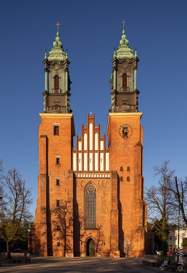 Zdjęcie przedstawia imponujący, ceglany budynek kościoła z dwoma wysokimi wieżami, które dominują nad główną nawą.