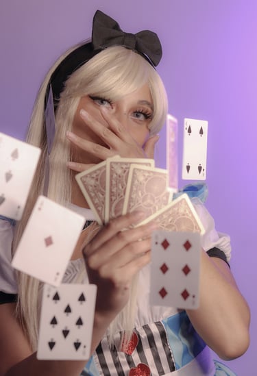 Playful costume of Alice in Wonderland holding playing cards, more cards floating in the air. 
