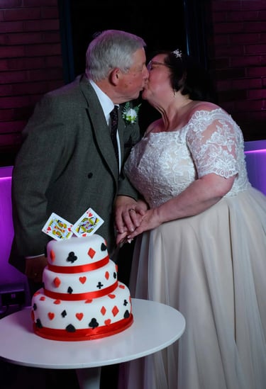 A bride and groom kiss behind a deck of cards themed wedding cake at their reception.