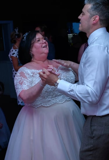 Smiling bride in lace wedding dress dancing with her son at a wedding reception.