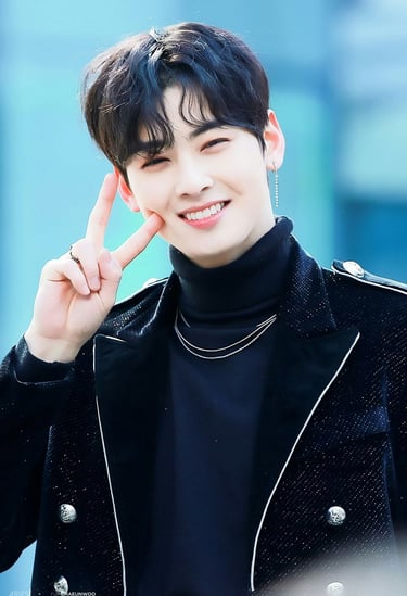 K-pop idol Cha Eun-woo smiling and making a peace sign in a black turtleneck and jacket.