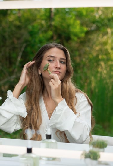 A woman uses a green jade roller for a facial massage and skincare routine.