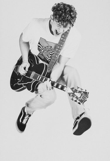 a man in a white shirt and tie dye on a guitar