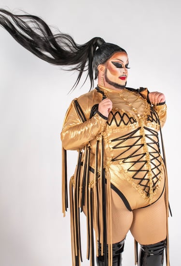 drag queen posing confidently in gold bodysuit with long tassles and hair whipping behind her