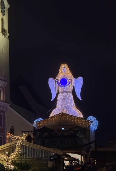 A large illuminated Christmas angel display glowing above rustic wooden stalls at the Wels Christmas