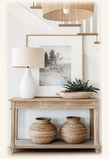 entrée intemporelle, console bois clair, pot en rotin dessous, plante verte, lampe blanche et tableau  dessus, suspension en 