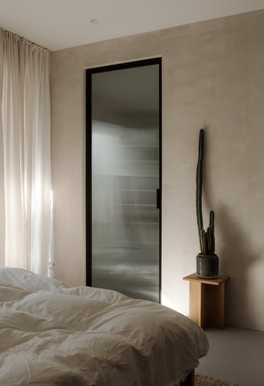 Bedroom with textured wall, fluted glass door, and white linens