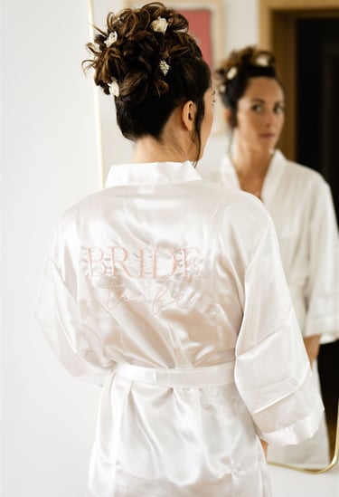 Bride in robe marked 'Bride' looking in mirror — fine art wedding preparation in South of France