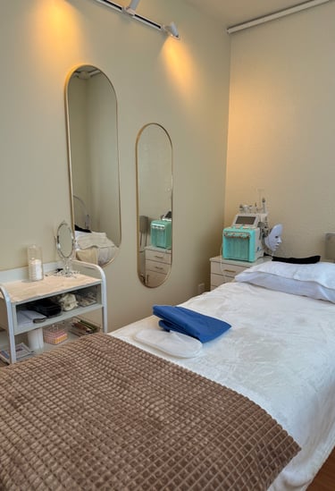 Professional facial treatment room featuring a medical spa bed, oval mirrors, and hydra-facial machine.