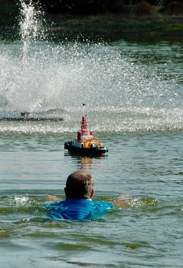 Man swimming in lake toward model tugboat