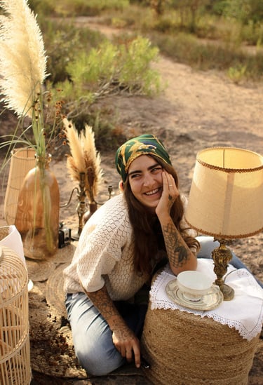 Margot Dubs Tattoo sourit, entouré d'une lampe et d'un vase, dans une lumière chaude