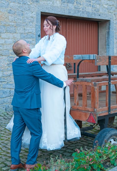 Un marié en costume bleu aide une mariée en robe blanche à descendre d'une calèche 