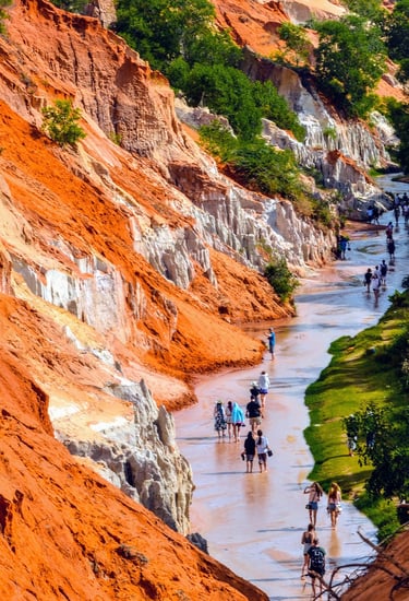 Tourists walking through the Fairy Stream (Suoi Tien) in Mui Ne with red sand cliffs on the left and