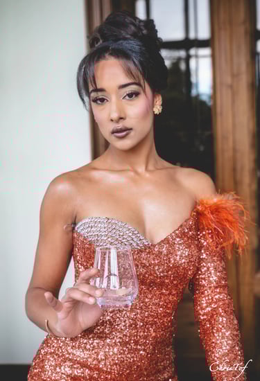 Photo à Perpignan d'une femme élégante en robe orange tenant un verre, chignon haut et maquillage