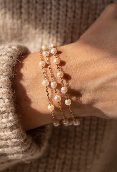 Elegant woman's wrist wearing three delicate 14k gold chain bracelets with cultured white pearls.