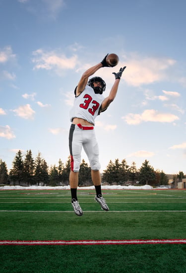 A football player in a white and red jersey jumps to catch a football on a green field.