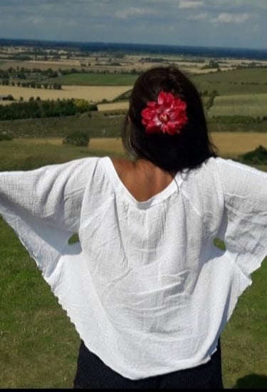 An image of the back of Sheila Cristina on the top of a hill. In front of her is a beautiful view of many fields in England.