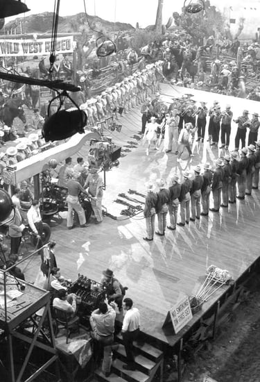 Behind‑the‑scenes shot of Berkeley filming Judy Garland and Mickey Rooney with fanned‑out cowboy dan