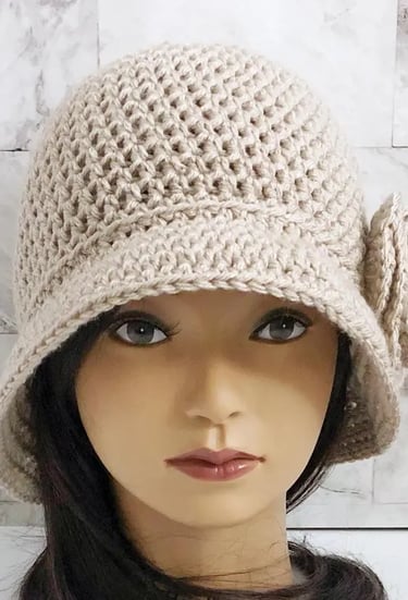 Woman wearing a tan crochet cloche hat with a large brim and flower on the side.