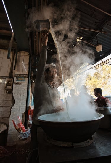 ea vendor pouring hot chai from height at a street stall in Old Delhi.