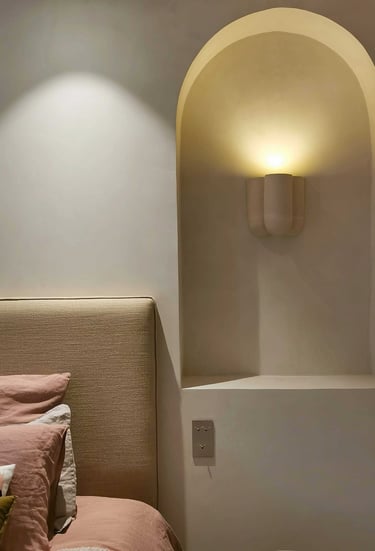 Modern minimalist bedroom featuring a beige upholstered headboard and a curved wall niche with a warm wall sconce.