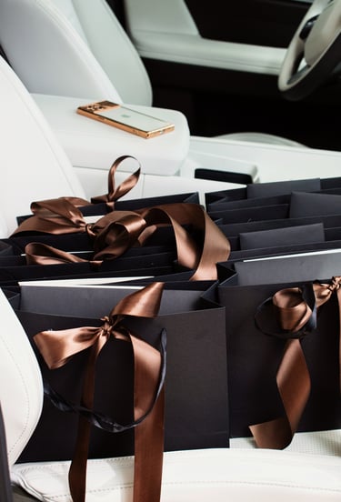 Luxury black shopping bags with satin brown ribbons on a white leather car seat.