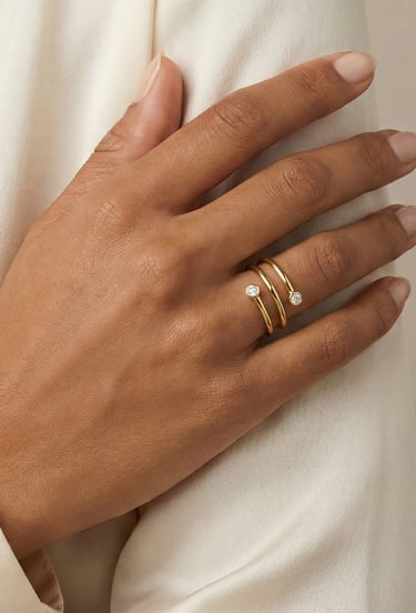 Una persona que lleva en el dedo un anillo envolvente de oro de 14 quilates con dos diamantes redond