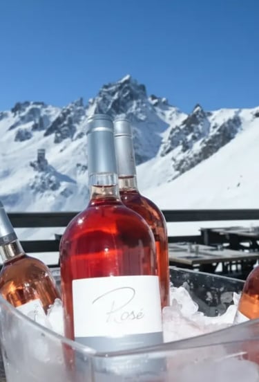 Bottles of rosé wine chilled in an ice bucket with a panoramic view of snow-capped Alpine peaks in t
