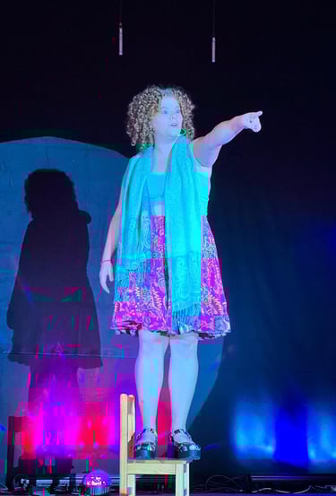 ein lockiges Mädchen auf einem Stuhl stehend im Spotlight auf der Bühne