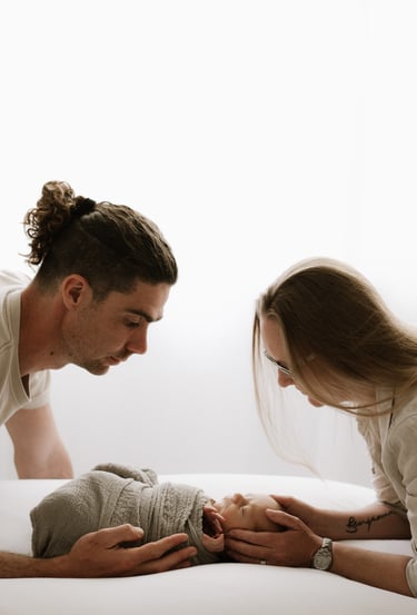newborn photographed with his mom & dad looking down in front of a window in Adelaide Hills