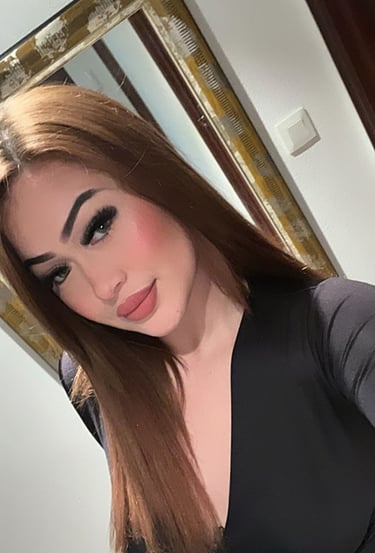 Joven escort de rostro definido y maquillaje sofisticado, con vestido negro escotado en un selfie frente al espejo.