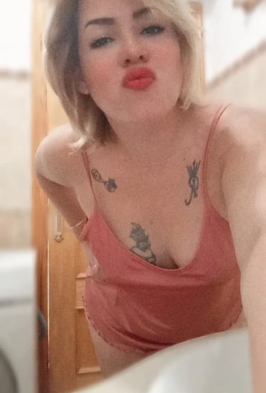 Selfie de Nikol con pijama rosa, labios sensuales y tatuajes visibles en el pecho
