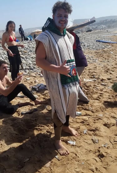 Smiling man wearing a traditional striped djellaba and face paint on a sunny beach.