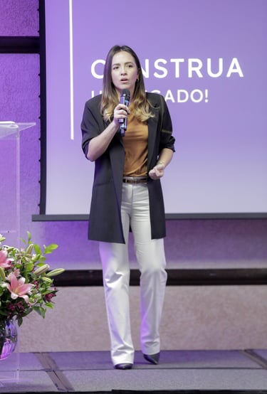uma mulher em pé encima de um palco, em frente a um projetor de imagens com um microfone