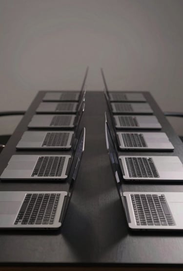 Symmetrical shot of a neat row of identical space gray MacBook Pros on a clean black workbench, edge-lit studio lighting.