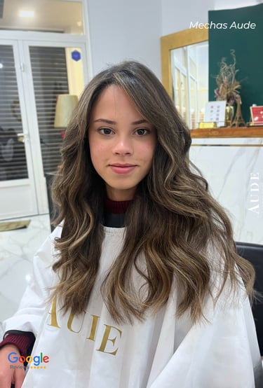 Young woman with long, wavy brown hair and blonde balayage highlights styled at a professional salon.