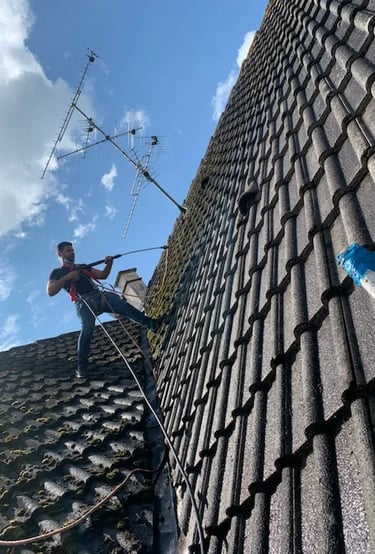 Artisan couvreur en intervention sur une toiture, effectuant un nettoyage haute pression à Belfort, équipé de harnais de sécu