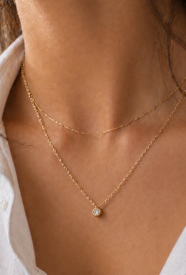 Close-up of delicate gold chain necklace with small pendant layered on simple outfit