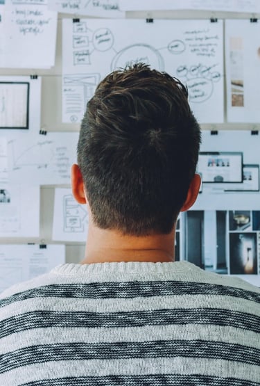 Persona espalda, suéter rayas, mirando tablero ideas.